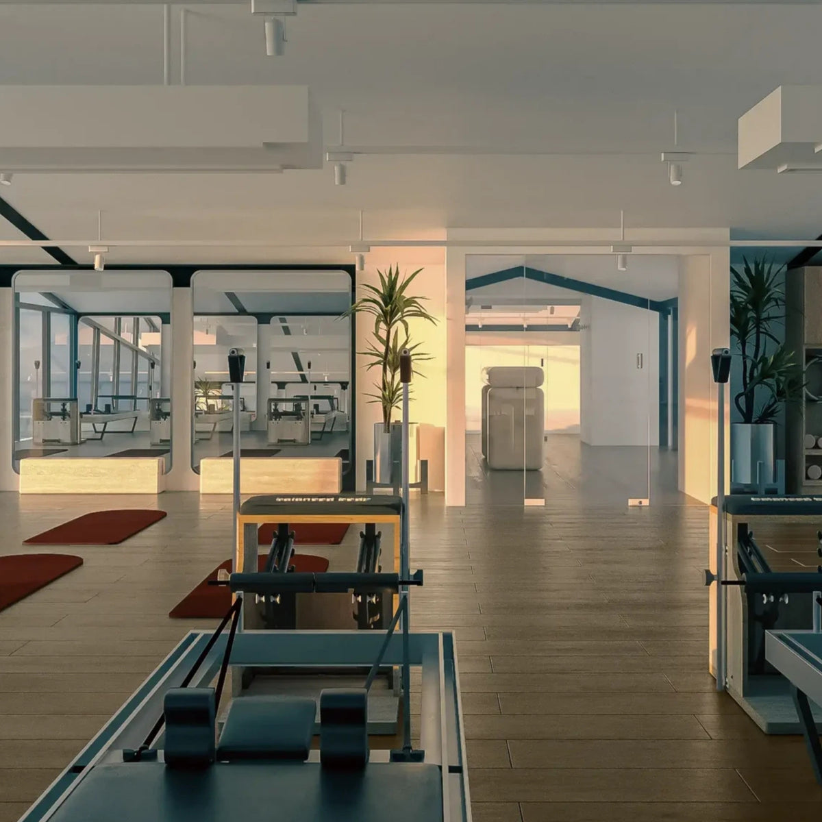 Pilates reformer machines in a bright, modern fitness studio with wooden floors, large windows, and warm natural light.