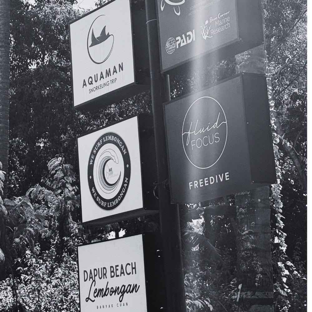 Collection of signs with various local brand logos against on a street corner of Nusa Lembongan