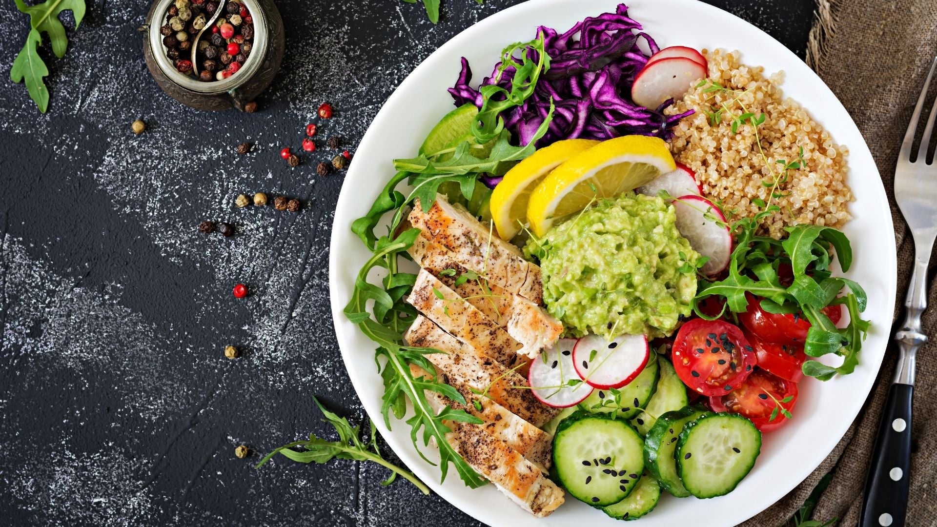 Plated salad with fish, vegetables, and guacamole on a dark surface