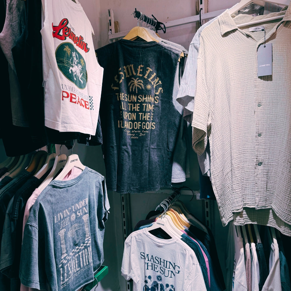 Collection of t-shirts on hangers with various designs and text in store at Island Paradise Outlet in Nusa Lembongan