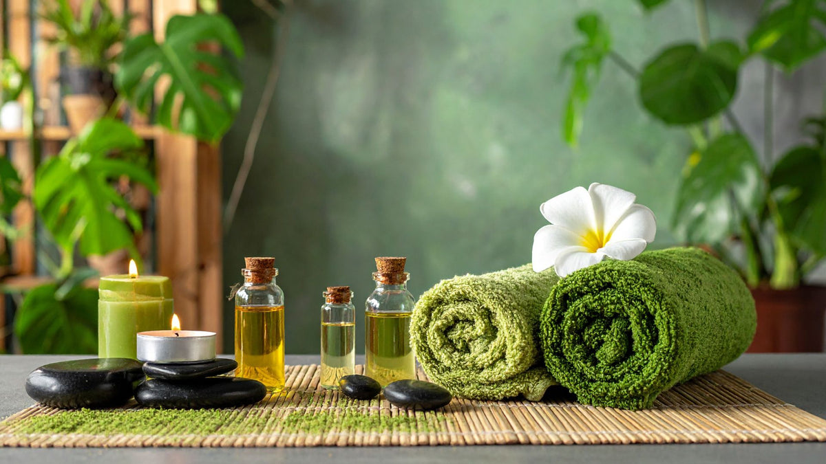 Green towels, candles, and bottles on a table with plants in the background inside a Massage Studio in Nusa Lembongan