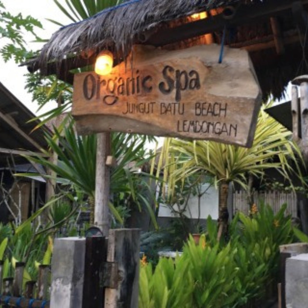A rustic wooden sign reading 'Organic Spa' with 'Jungut Batu Beach Lembongan' underneath, mounted on a post in front of tropical plants and a thatched roof.
