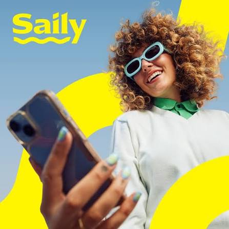 A smiling woman with curly hair, light blue sunglasses, and a green collar wears a white top while holding a smartphone. The background is a bright blue graphic with large yellow shapes and the word 'Saily' in yellow at the top left promoting Saily eSim