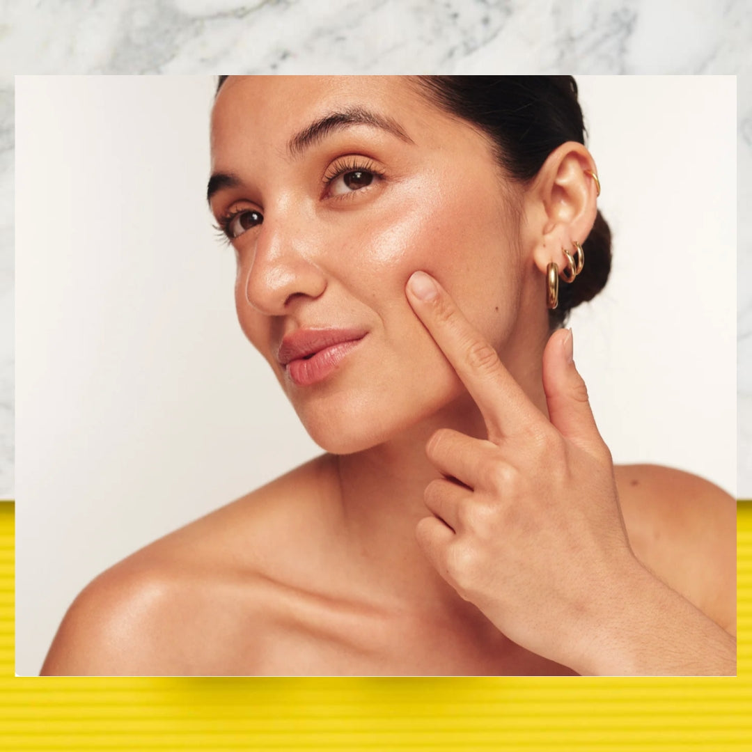 A close-up lifestyle shot of a woman with radiant skin touching her cheek, wearing small gold hoop earrings. The photo is framed within a white border with a yellow textured stripe at the bottom.