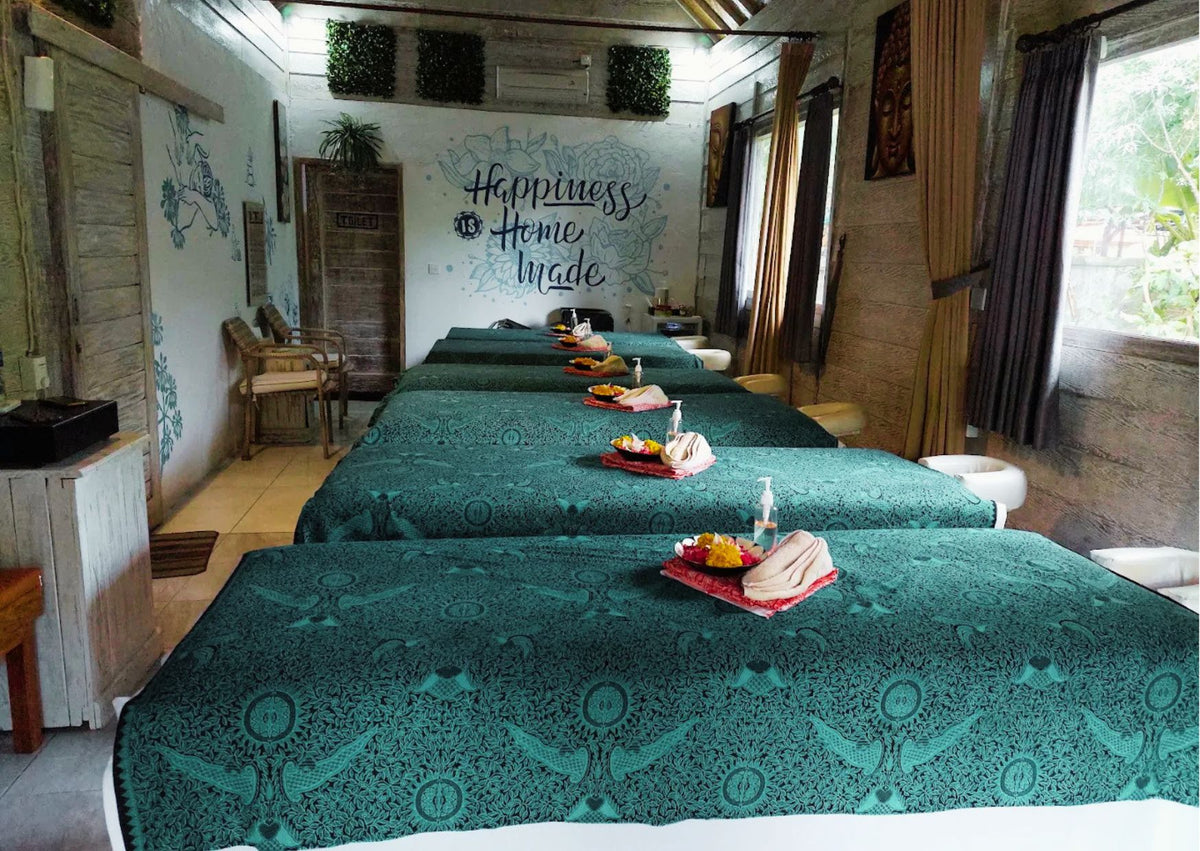 The massage treatment room of Syron Spa in Mushroom Bay, with multiple massage tables covered in teal patterned sheets, arranged in parallel rows. 