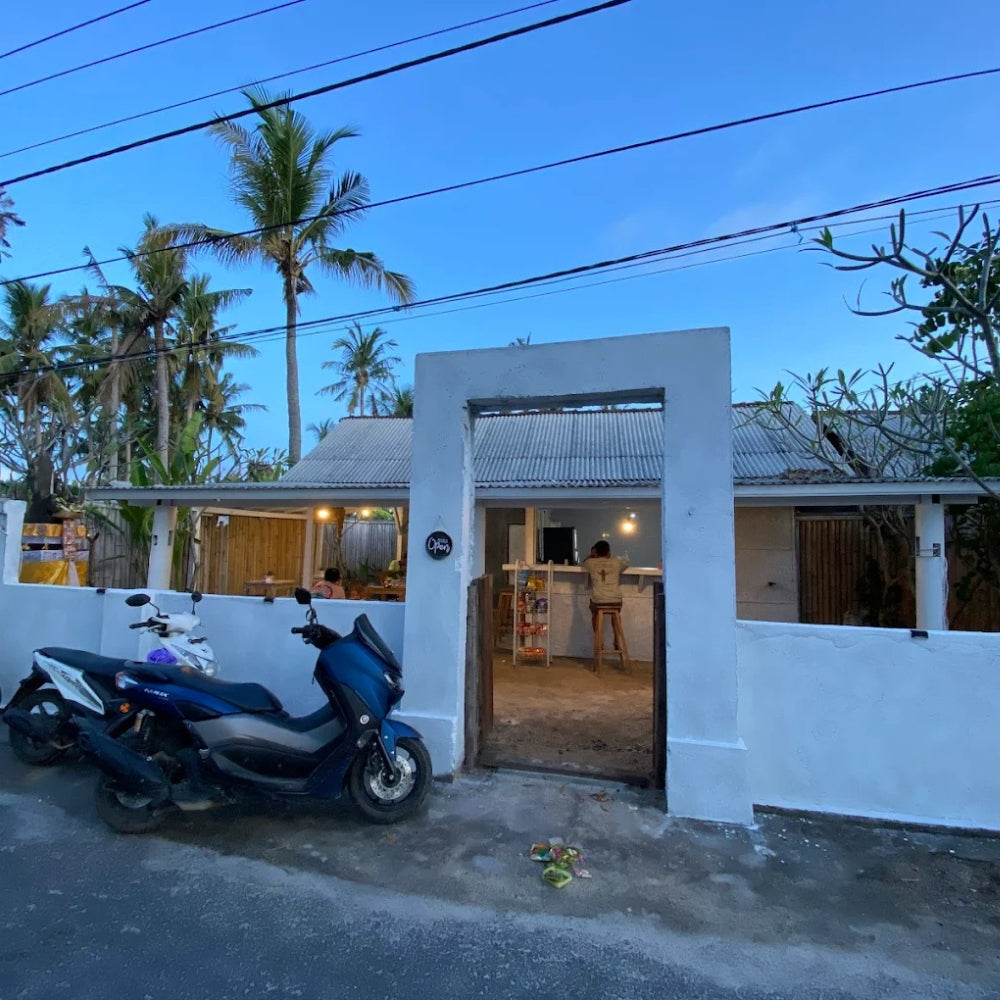 The outside exterior of local Warung ID with a white wall and open door, parked scooters on the left, located in Nusa Lembongan